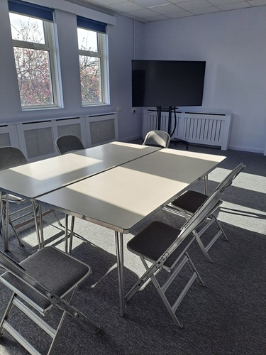Eccleshill Library meeting room with tables and chairs and a screen in the corner by a window.